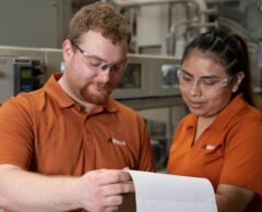 Two factory workers in orange shirts examining a piece of paper