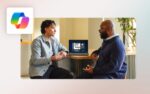 Two employees talking in front of a laptop with a M365 Copilot logo floating above
