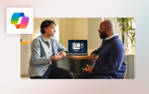 Two employees talking in front of a laptop with a M365 Copilot logo floating above